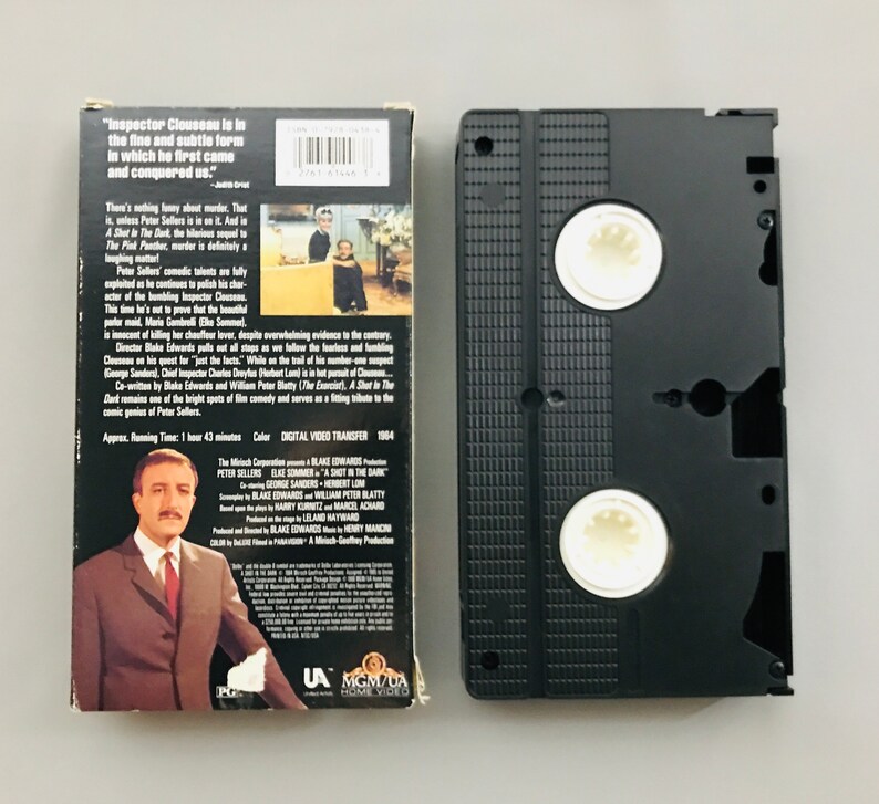 May include: A VHS tape case with a black background and a white label. The label features a photo of Peter Sellers, the title "A Shot in the Dark", and the text "Inspector Clouseau is in the fine and subtle form in which he first came and conquered us."
