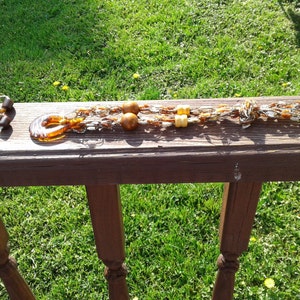 May include: A brown and gold beaded necklace with wooden beads and a brown glass pendant. The necklace is on a wooden surface.