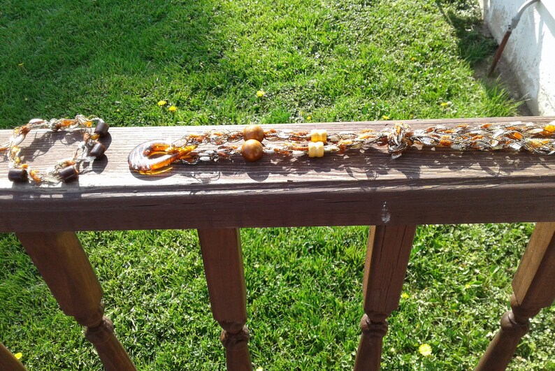 May include: A brown and gold beaded necklace with wooden beads and a brown glass pendant. The necklace is on a wooden surface.