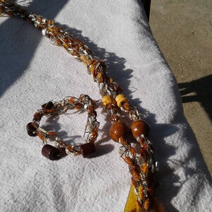 May include: A brown and white crocheted necklace with wooden beads and a large amber glass pendant. A matching crocheted bracelet with brown beads is also included.
