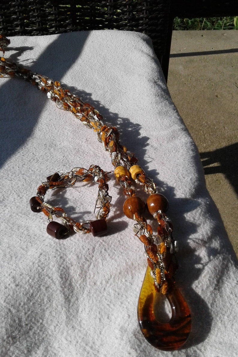May include: A brown and white crocheted necklace with wooden beads and a large amber glass pendant. A matching crocheted bracelet with brown beads is also included.