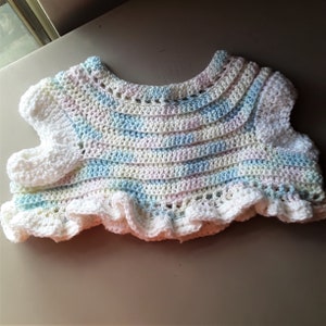 May include: A crocheted baby top with a ruffled hem and pastel stripes. The top is made with white and light blue yarn.