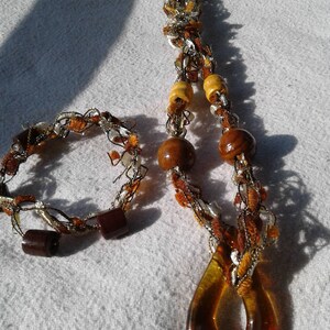 May include: A brown and white crocheted necklace with wooden beads and a teardrop-shaped amber pendant.