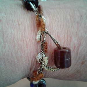 May include: A brown and black beaded bracelet with gold and white accents. The bracelet is made with a variety of materials, including beads, yarn, and string.