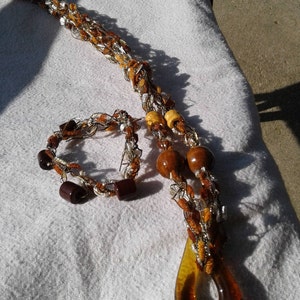 May include: A brown and gold crocheted necklace with wooden beads and a brown glass pendant. A matching brown and gold crocheted bracelet is also included.