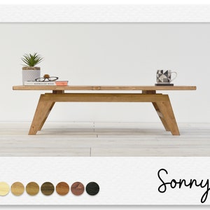 May include: A light wood coffee table with a simple design. The table has a rectangular top and four legs. The legs are angled and have a slightly flared shape. The table is sitting on a light wood floor. The table is decorated with a potted plant, a book, and a mug.