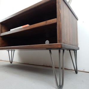 May include: A dark brown wooden TV stand with a blue door and a shelf. The stand has hairpin legs and is sitting on a light grey floor.