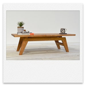 May include: A wooden coffee table with a natural finish. The table has a rectangular top and a simple, mid-century modern design. It features a lower shelf and angled legs.