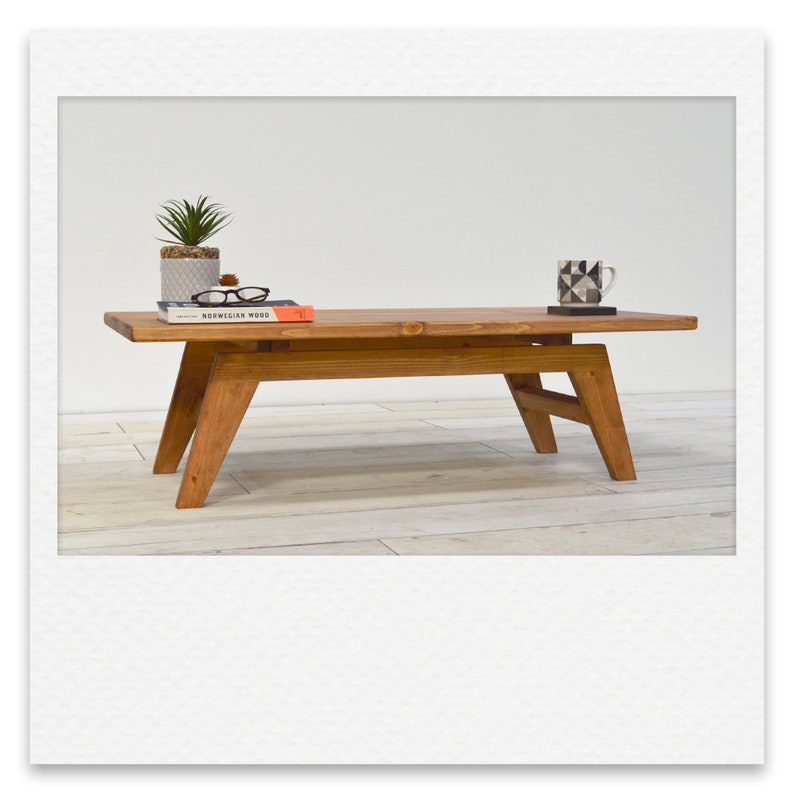 May include: A wooden coffee table with a natural finish. The table has a rectangular top and a simple, mid-century modern design. It features a lower shelf and angled legs.