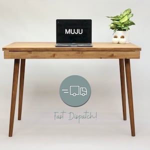 May include: A light wood desk with a laptop on top. The laptop screen displays the word "MUJU". The desk has a drawer and tapered legs. A potted plant sits on the desk to the right of the laptop.
