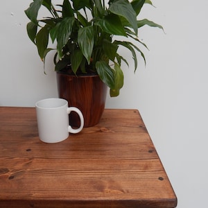 May include: A wooden table with a yellow drawer and a black knob. The table top is stained a dark brown colour. A white mug and a potted plant are on the table.