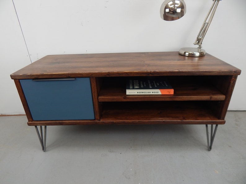May include: A dark brown wooden coffee table with a blue painted drawer and two shelves. The table has hairpin legs and a book titled "Norwegian Wood" on the top shelf.