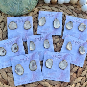 May include: A set of eight pairs of handmade ceramic earrings. Each pair features a unique, irregular shape with a white glaze and gold accents. The earrings are displayed on cards with the text "s.a.l.t." and "handcrafted in Charleston, SC".