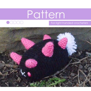 May include: Crochet pattern for a black and pink spiky creature with a white fluffy tail. The pattern is for right-handed crocheters.