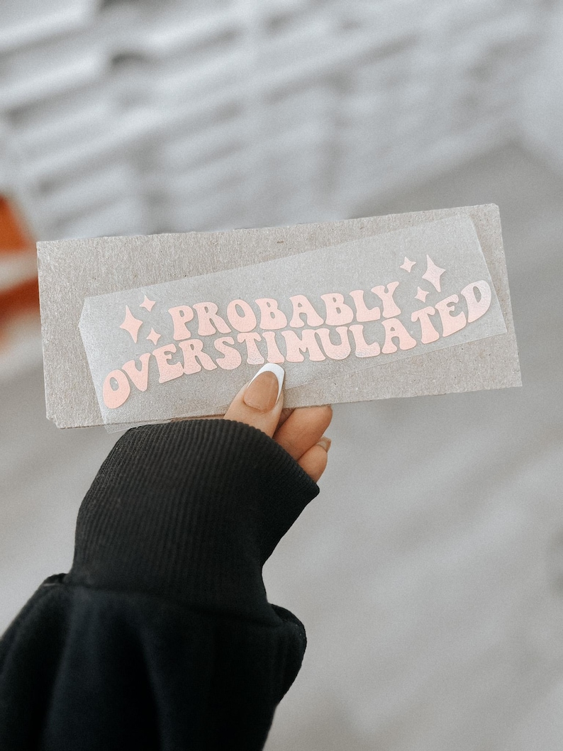 May include: A pink and white sticker with the text "PROBABLY OVERSTIMULATED" in a retro font style.