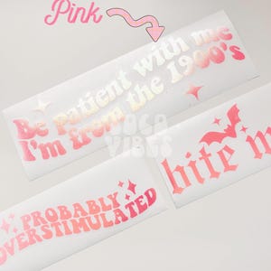 May include: Three holographic pink vinyl stickers with different phrases. The first sticker says "Be patient with me I'm from the 1900's". The second sticker says "Probably Overstimulated". The third sticker says "bite me".