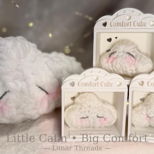 May include: A plush white cloud with a smiling face and pink cheeks, next to three smaller cloud-shaped Comfort Cubes in decorative boxes. The text "Little Calm • Big Comfort" and "Lunar Threads" is visible.
