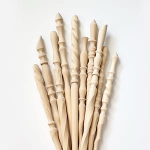 May include: A collection of 13 wooden dowels with various carved designs and finishes. The dowels are all natural wood color and have different shapes and sizes.