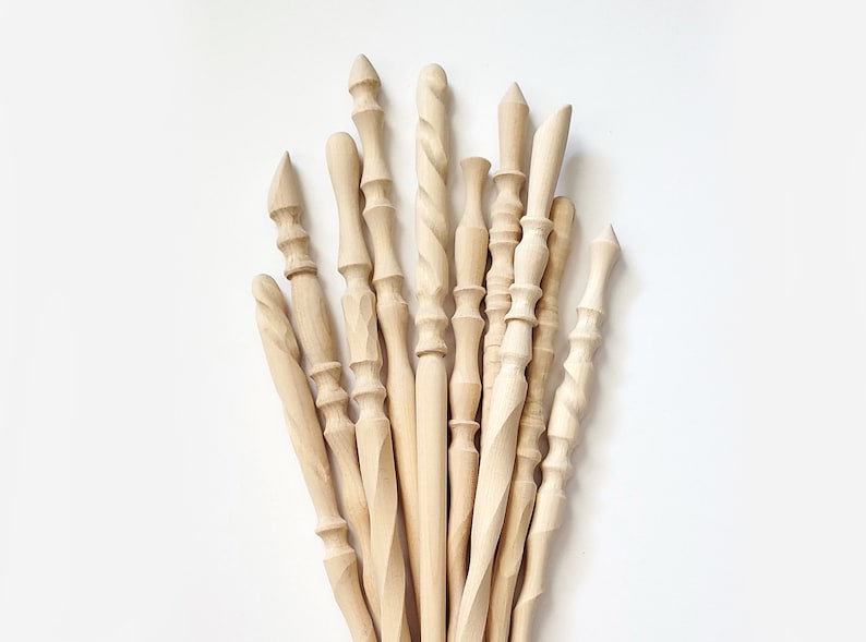 May include: A collection of 13 wooden dowels with various carved designs and finishes. The dowels are all natural wood color and have different shapes and sizes.