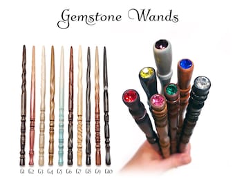 Puede incluir: Una colección de diez varitas de madera etiquetadas de G1 a G10, con varios tonos y texturas de madera. A la derecha, un grupo de varitas con piedras preciosas facetadas de colores incrustadas en los mangos, incluyendo rojo, amarillo, rosa, verde, azul y transparente.