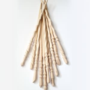 May include: A collection of 12 unfinished wooden wands, each with a unique shape and design. The wands are made of natural wood and have a smooth, polished finish.