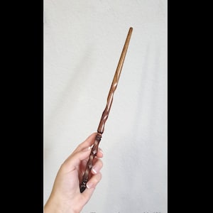 Puede incluir: Una varita de madera de color marr&oacute;n oscuro con un mango retorcido en espiral y un eje liso y c&oacute;nico. La varita tiene un acabado pulido y mide aproximadamente 30,48 cm de largo, seg&uacute;n indica el texto impreso en la parte inferior.