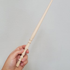 May include: A plain wooden wand with a rounded tip and a detailed handle. The wand is held in a hand.