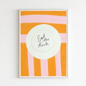 Op de afbeelding: Een ingelijst print met een wit bord in het midden. Het bord heeft de tekst "Eat the Rich" erop geschreven. De achtergrond is oranje en roze strepen.