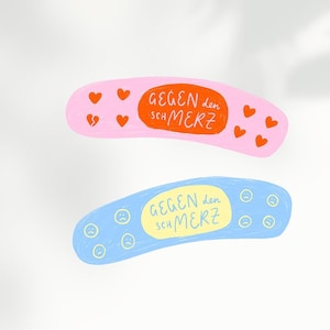 Könnte beinhalten: Zwei bunte Pflaster-förmige Aufkleber mit dem Text "GEGEN den SCHMERZ" in Orange. Der rosa Aufkleber hat gebrochene Herzen und der blaue Aufkleber hat traurige Gesichter.