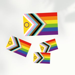 Puede incluir: Cuatro banderas del orgullo coloridas con fondo amarillo y un círculo morado en el centro. Las banderas están dispuestas de forma dispersa sobre un fondo blanco.