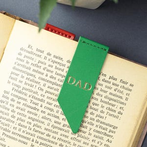 May include: Green leather bookmark with the gold embossed word "DAD". The bookmark is inserted into a book with printed text. A red leather bookmark is also visible.