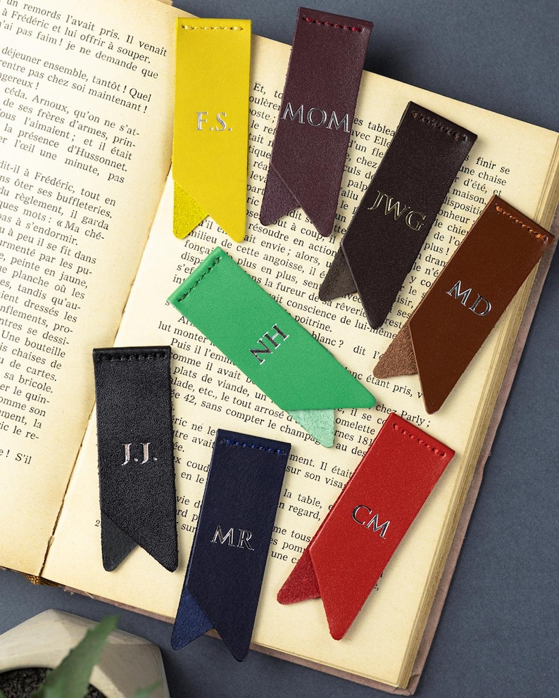 May include: A selection of leather bookmarks in different colours, each featuring silver embossed initials. The bookmarks are displayed on the pages of an open book, highlighting a range of shades.