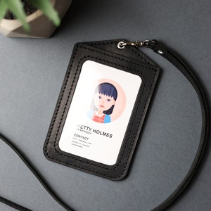 May include: Black leather ID badge holder with a clear plastic window for a photo and a black lanyard. The holder has a stitched border and the text "KETY HOLMES, HR MANAGER, CONTACT, KETY.HOLMES@MAIL.COM, DUPAIO CO. UKRAINE, +380999999999" is printed on the card inside the window.