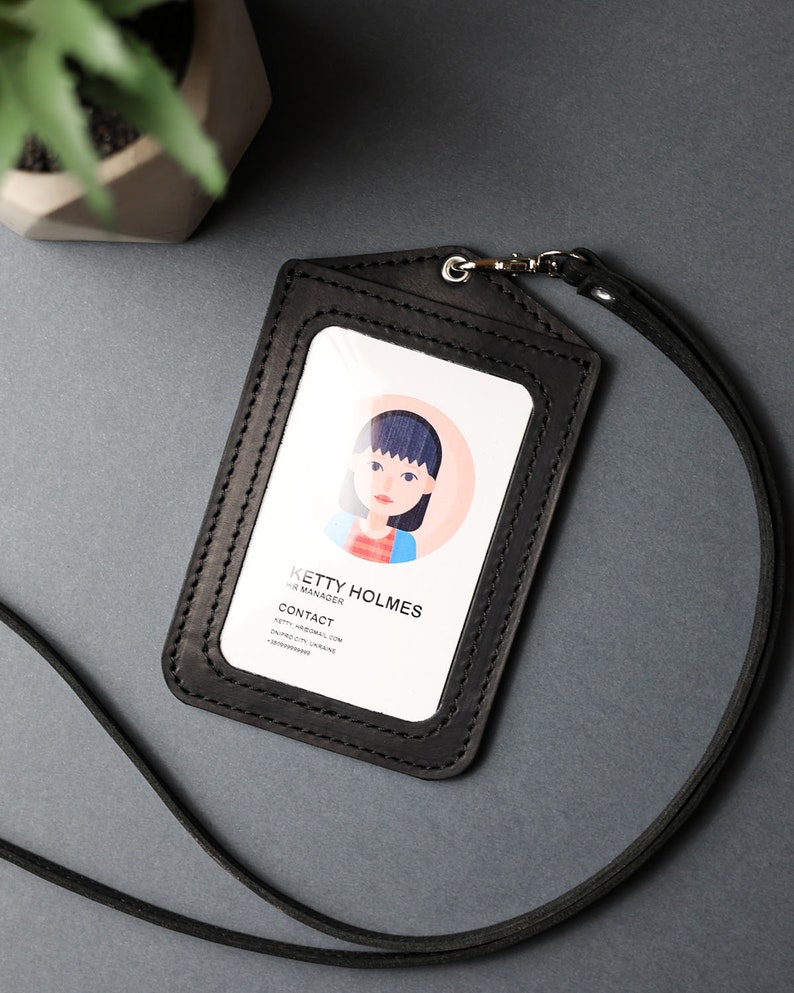 May include: Black leather ID badge holder with a clear plastic window for a photo and a black lanyard. The holder has a stitched border and the text "KETY HOLMES, HR MANAGER, CONTACT, KETY.HOLMES@MAIL.COM, DUPAIO CO. UKRAINE, +380999999999" is printed on the card inside the window.