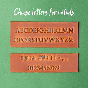 May include: Two brown leather strips with black lettering. The top strip has the alphabet in uppercase letters. The bottom strip has symbols, numbers, and the word "No".
