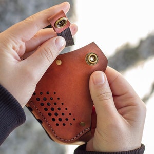 May include: A brown leather mask with a perforated design and brass accents. The mask has a strap that attaches with a snap.