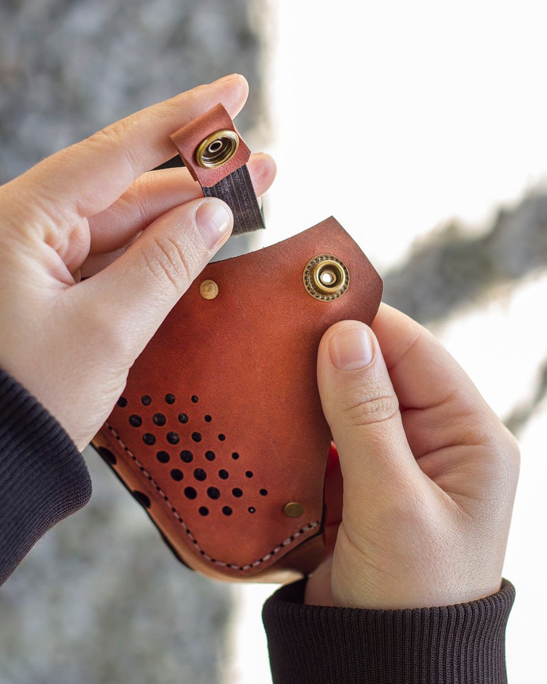 May include: A brown leather mask with a perforated design and brass accents. The mask has a strap that attaches with a snap.