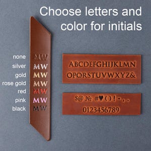 May include: A brown leather bookmark with the text "Choose letters and color for initials." The bookmark has the letters "MW" in various colours, including silver, gold, rose gold, red, pink, and black. Alphabet and number samples are also shown.