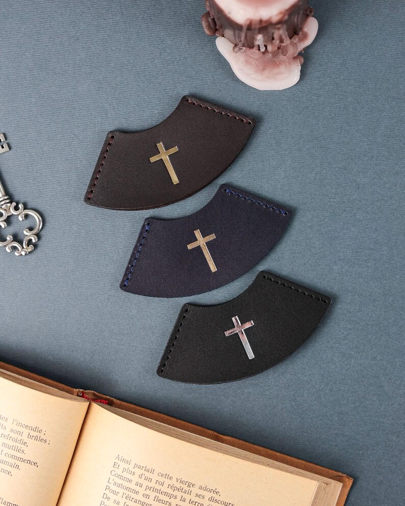 May include: Three leather bookmark corner tabs with a silver cross design. The bookmarks are in brown, dark blue, and black.