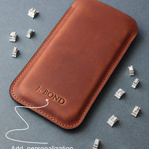 May include: A brown leather phone case with the text "J. BOND" embossed on the front. The case is shown with metal letter stamps for personalization.