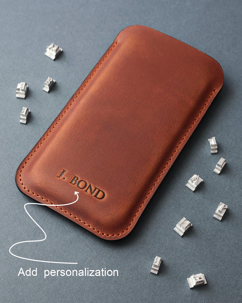 May include: A brown leather phone case with the text "J. BOND" embossed on the front. The case is shown with metal letter stamps for personalization.