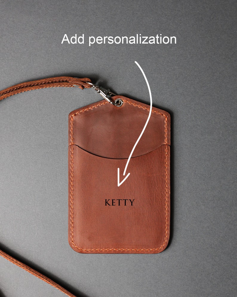 May include: A brown leather ID card holder with a strap. The holder has a pocket for cards and a space for personalization. The text "KETTY" is embossed on the front.
