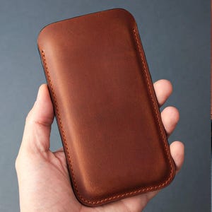 May include: A brown leather phone case with a stitched edge.