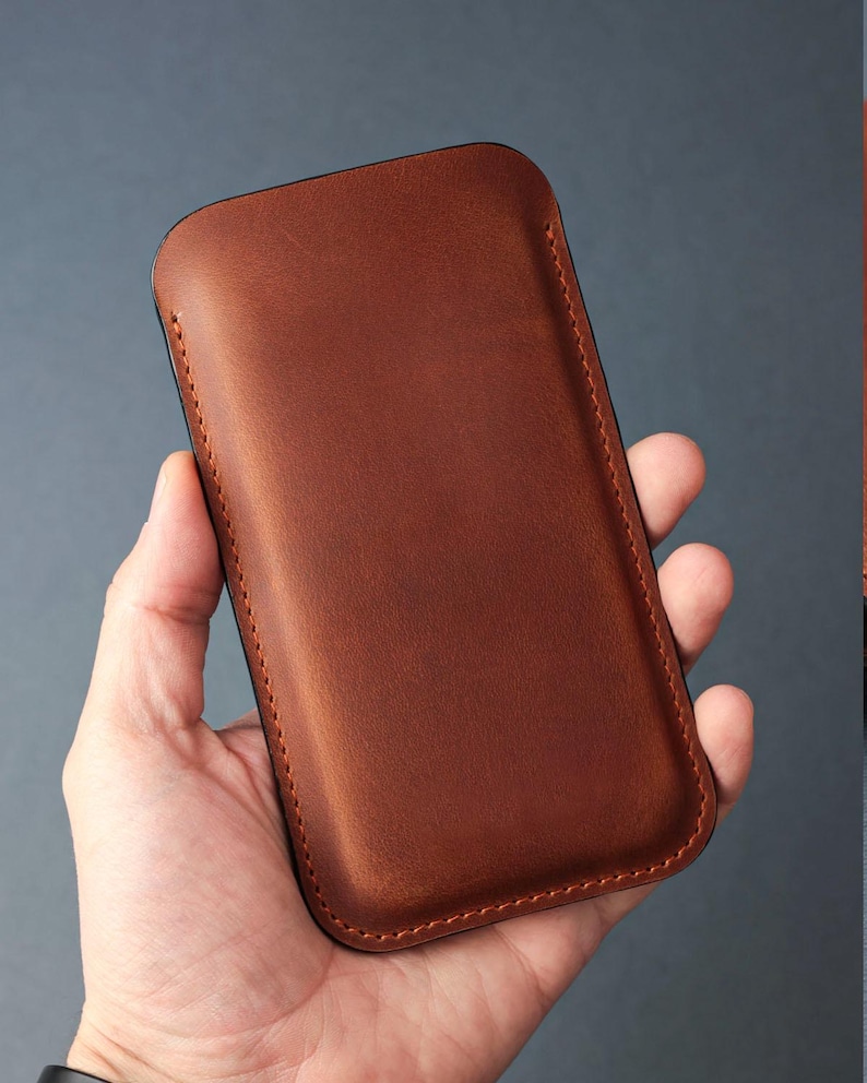 May include: A brown leather phone case with a stitched edge.