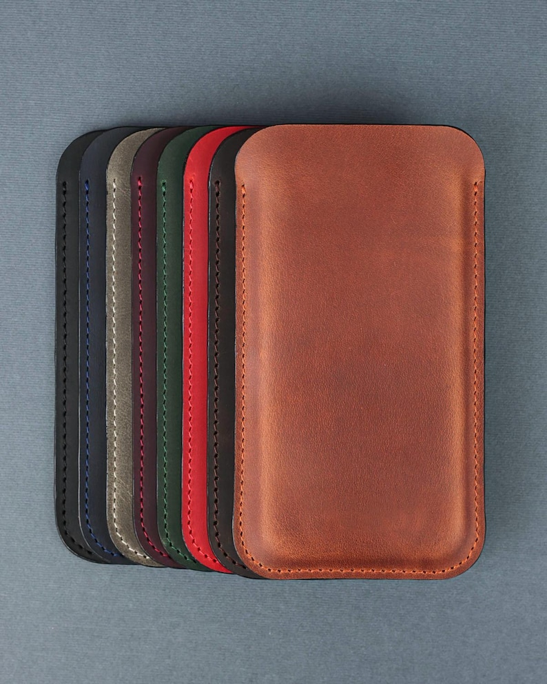 May include: A set of eight leather phone cases in various colors, including navy blue, gray, burgundy, green, red, black, and brown. The cases are lined up in a row, with the brown case at the front.