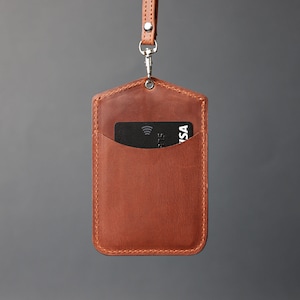 May include: A brown leather ID badge holder with a black card inside. The holder has a stitched edge and a silver chain attached to the top.