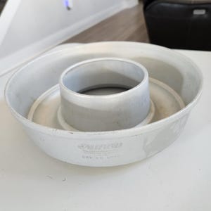 Puede incluir: Molde para bizcocho Bundt de aluminio gris claro con un tubo central y una base circular. El molde tiene un aspecto ligeramente desgastado. Diseñado para hornear pasteles y otros postres.
