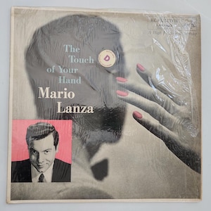 May include: Vintage vinyl record album cover for "The Touch of Your Hand" by Mario Lanza. The cover features a black and white image of a woman's hand with pink nail polish, and a portrait of Mario Lanza.