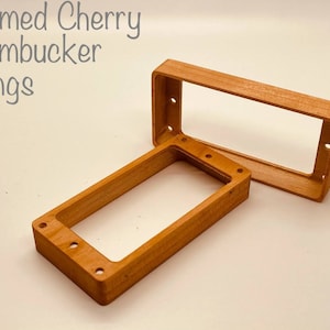May include: Two wooden humbucker rings in a flamed cherry finish. The rings are stacked on top of each other.