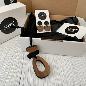May include: A gift box with a black and brown wooden necklace and earrings. The box is white with a black interior and the necklace and earrings are packaged on a black tissue paper. The box has a logo that says "LOVE designs by george" on the front.